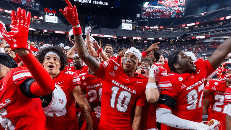 A football team celebrating on the field, wearing red uniforms, amidst cheering fans